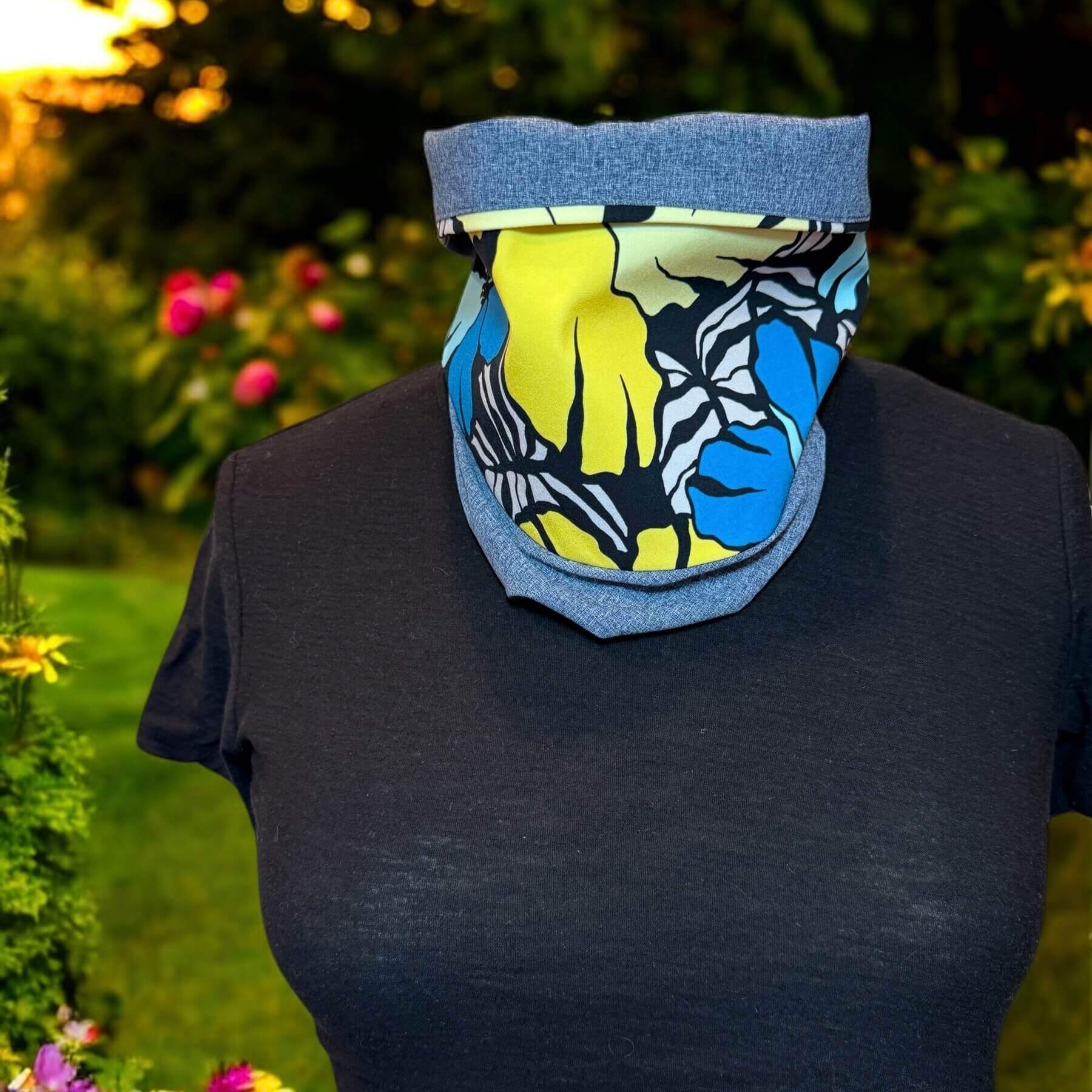 UV Sun Dickey with collar turned down peeks out of black James Perse t-shirt. In background is garden with grass, shrubs and flowers
