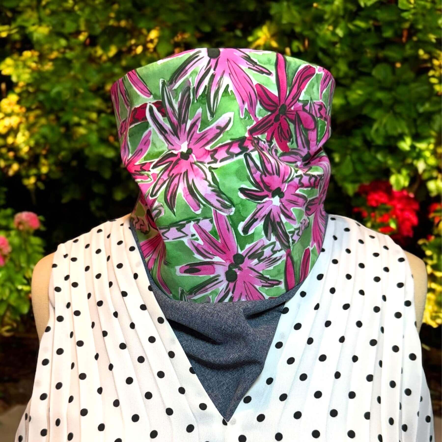 Fashion Sun Dickey in blue melange, green and pink palm tree print paired with black and white polka dot blouse from Banana Republic. In background is red flowers and green shrubs.