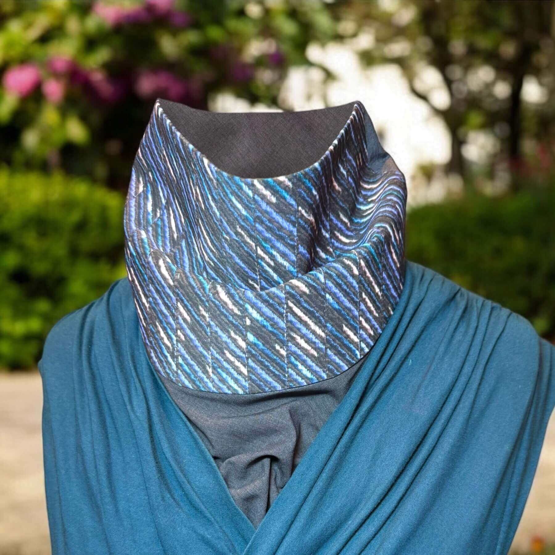 Sun Dickey shown on mannequin in charcoal gray melange with shades of blue, teal and white 'embroidered' (print) stripes in a diagonal pattern, paired with teal blue V-neck wrap front top. In background is backyard (blurred) with trees, flowers and shrubs.