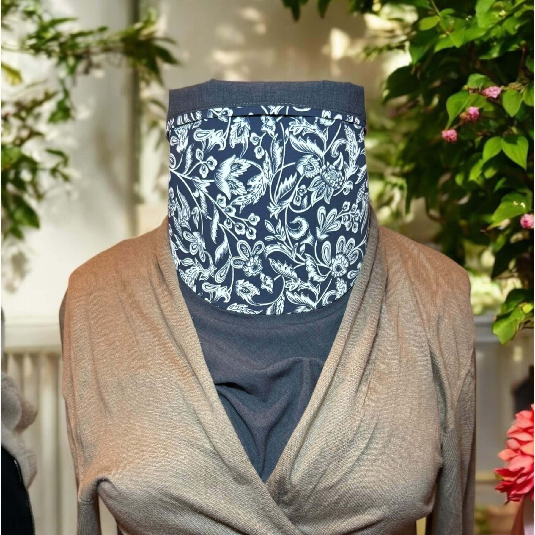 Pretty Sun Dickey is shown on mannequin in blue melange with intricate navy blue and white stylized floral pattern with leaves, flowers and scrolls and paired with a lightweight beige, V-neck sweater. Behind is garden with flowers and wall of house.