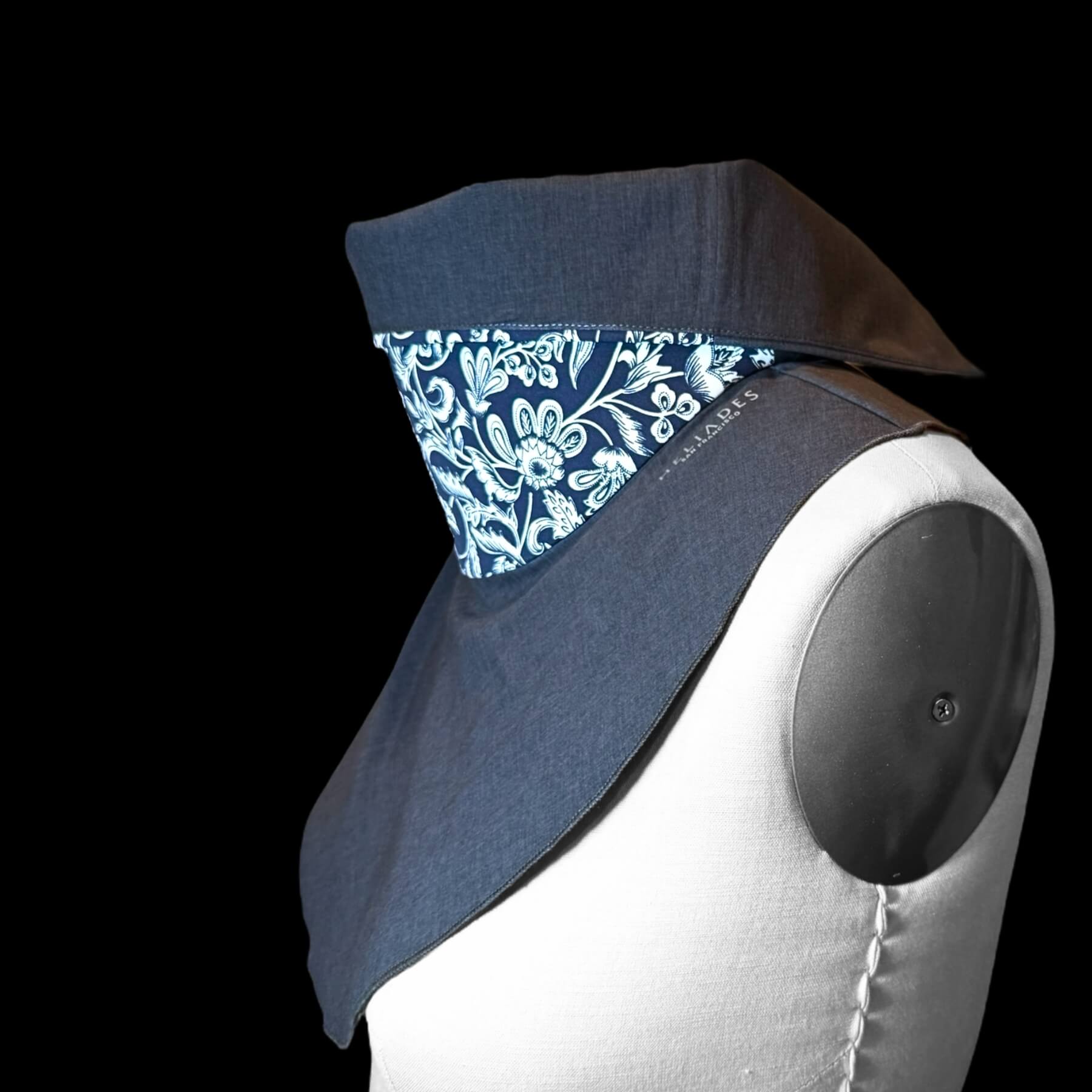 Chic UV Sun Dickey is shown on mannequin from side view with collar folded down to reveal contrast fabric. Sun Dickey colorway is blue melange with intricate navy blue and white stylized floral pattern with leaves, flowers and scrolls.