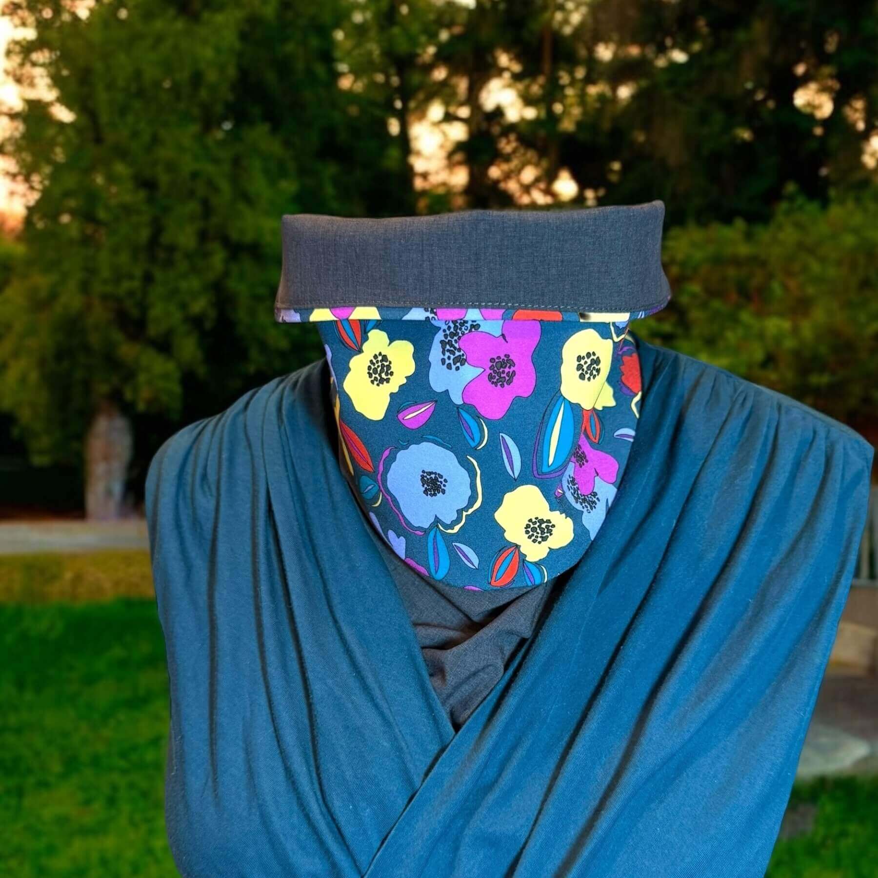Fashion Sun Dickey shown in charcoal gray melange with blue, violet, yellow and red floral print styled with a teal blue v-wrap blouse. Behind in the backyard are trees, grass and dirt.