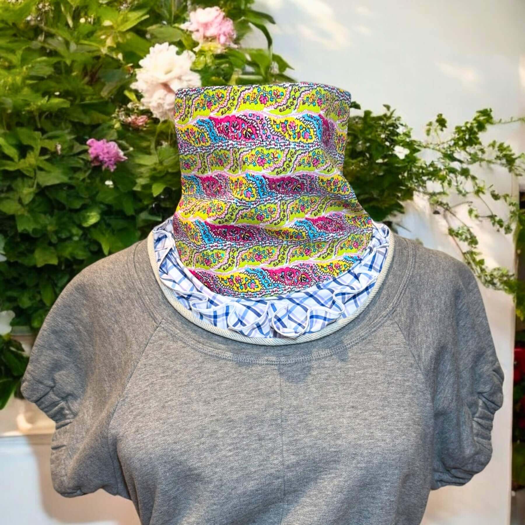 Blue, white plaid with pink, blue, green paisley print Sun Dickey shown paired with rolled jewel-collar gray Philip Lim sweatshirt. In background is white wall of backyard with green shrubs and pink flowers