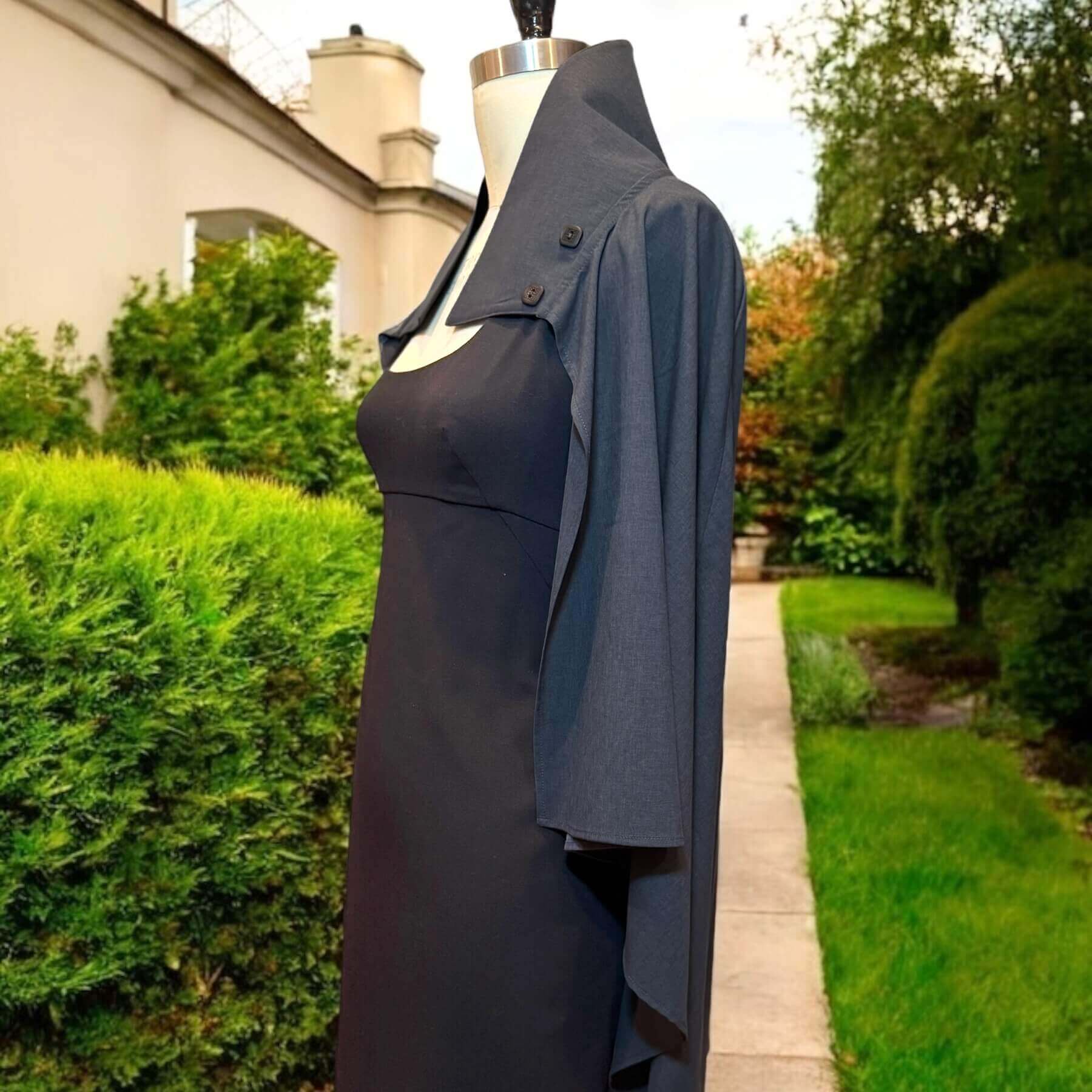 Side view of the Gray Melange Sun Shawl in UPF 50+ fabric, styled on a mannequin wearing a black scoop-neck evening dress. Photographed outdoors with grass, bushes, and a concrete walkway in the background.