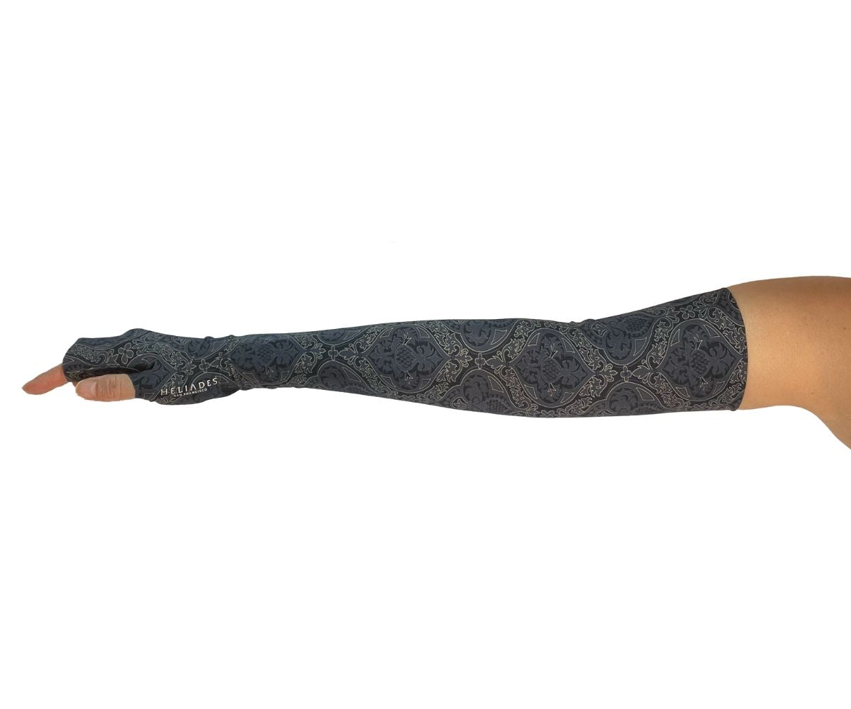 Heliades UPF 50 Sun Protective Clothing UV Arm Sleeves in fashionable, elegant allover black and gold print on a charcoal gray color. UV covered arm and hand shown with silver reflective logo trim.