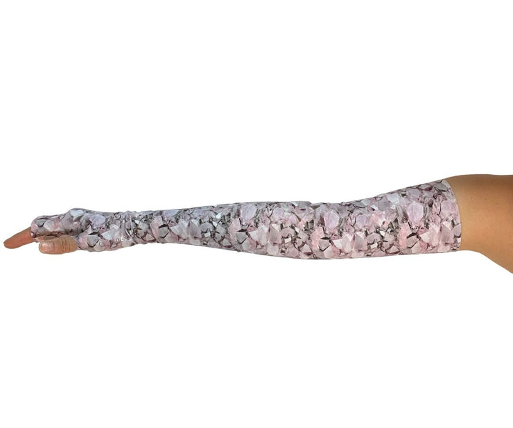 Heliades UPF 50 Sun Protective Clothing UV Arm Sleeves on stylish printed fabric. Shown in fashionable, elegant allover pink, white, lavender, magenta pattern. UV covered arm and hand shown with metallic pink logo trim