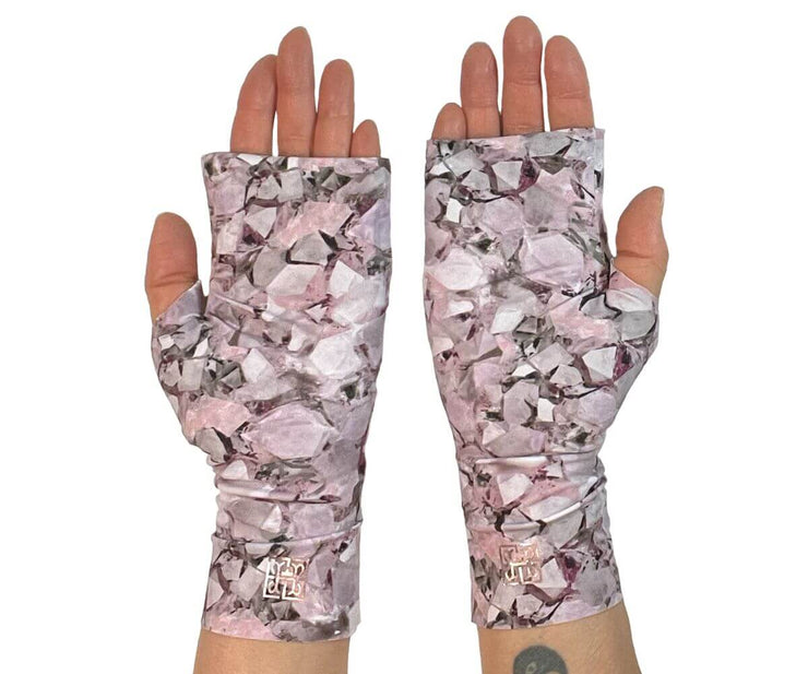 Heliades UPF 50 Sun Protective Clothing UV sun gloves on printed fabric. Shown is fashionable, elegant allover pink, lavender, white, magenta print. UV sun covered hands shown back with metallic pink logo trim