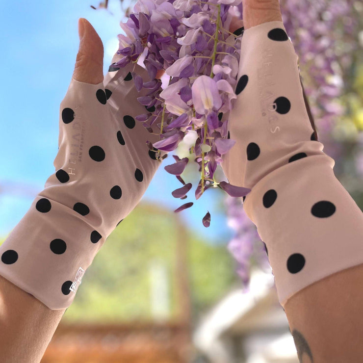 Hands wearing ballet pink with black polka dot UPF 50+ finger less sun gloves hold purple and lavender blooms of wisteria.