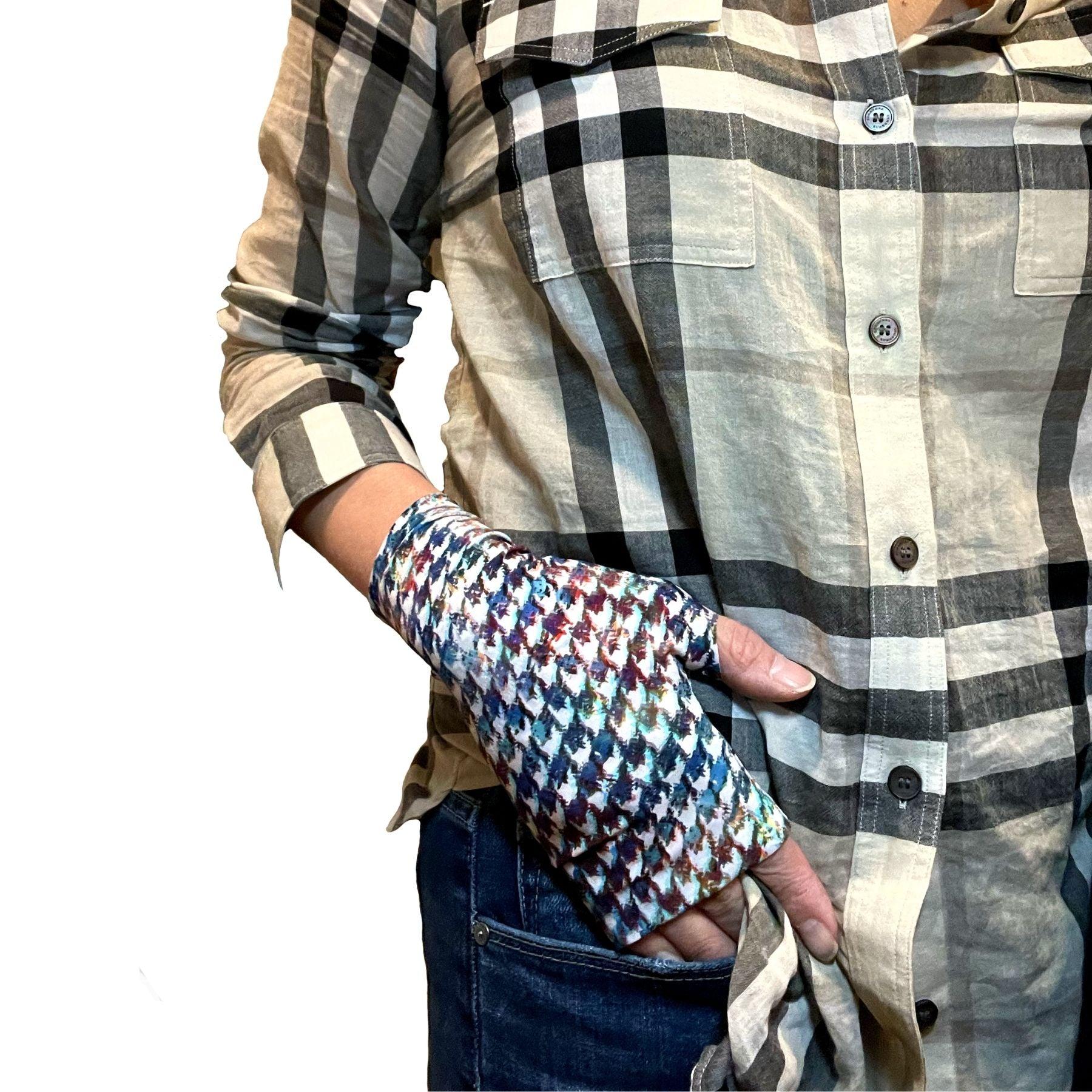Woman wearing Burberry check shirt and jeans. A hand rests on jeans pants pocket. On hand is best UPF 50+ sun protective fingerless sun gloves in multi-colored Painterly Houndstooth Plaid print made of UPF50+ and OEKO-TEX certified fabric. HELIADES logo shown, Made in USA.