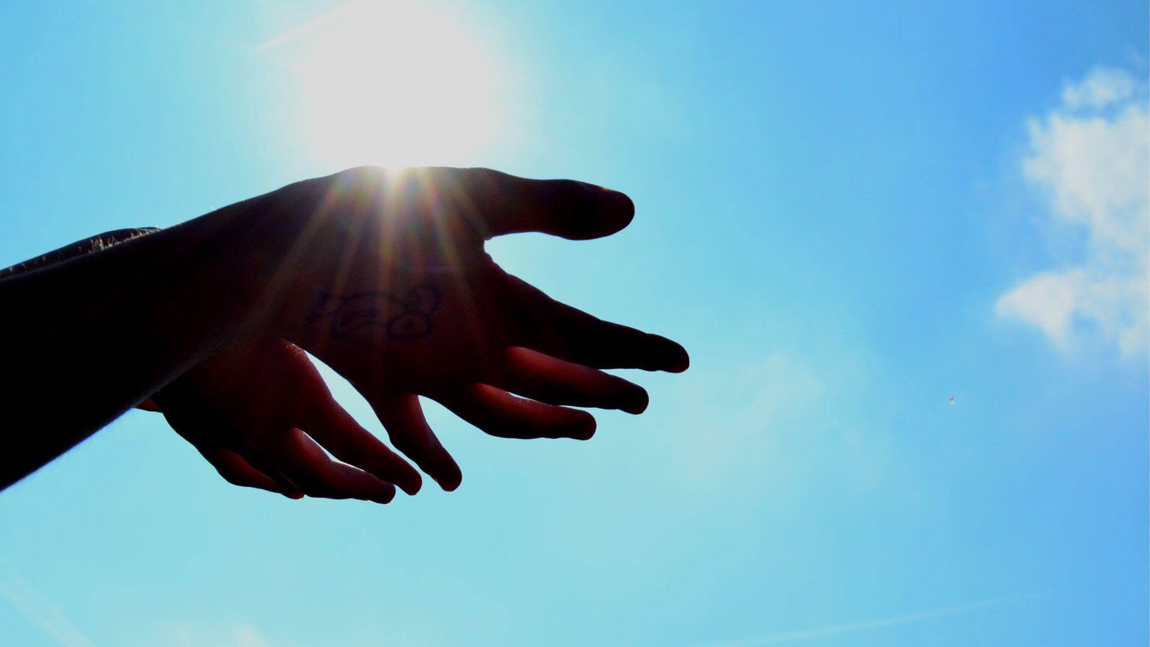 Heliades UPF Sun Protective Clothing, Gloves, Neck Wraps in stylish colors and prints with street appeal_Hands held outstretched to the sun with blue sky and clouds.