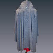 Back view of Sol Escape sun wrap shown in blue melange UPF50+ fabric. A red dress and the mannequin stand is visible at the bottom. Color background is blue gradient.