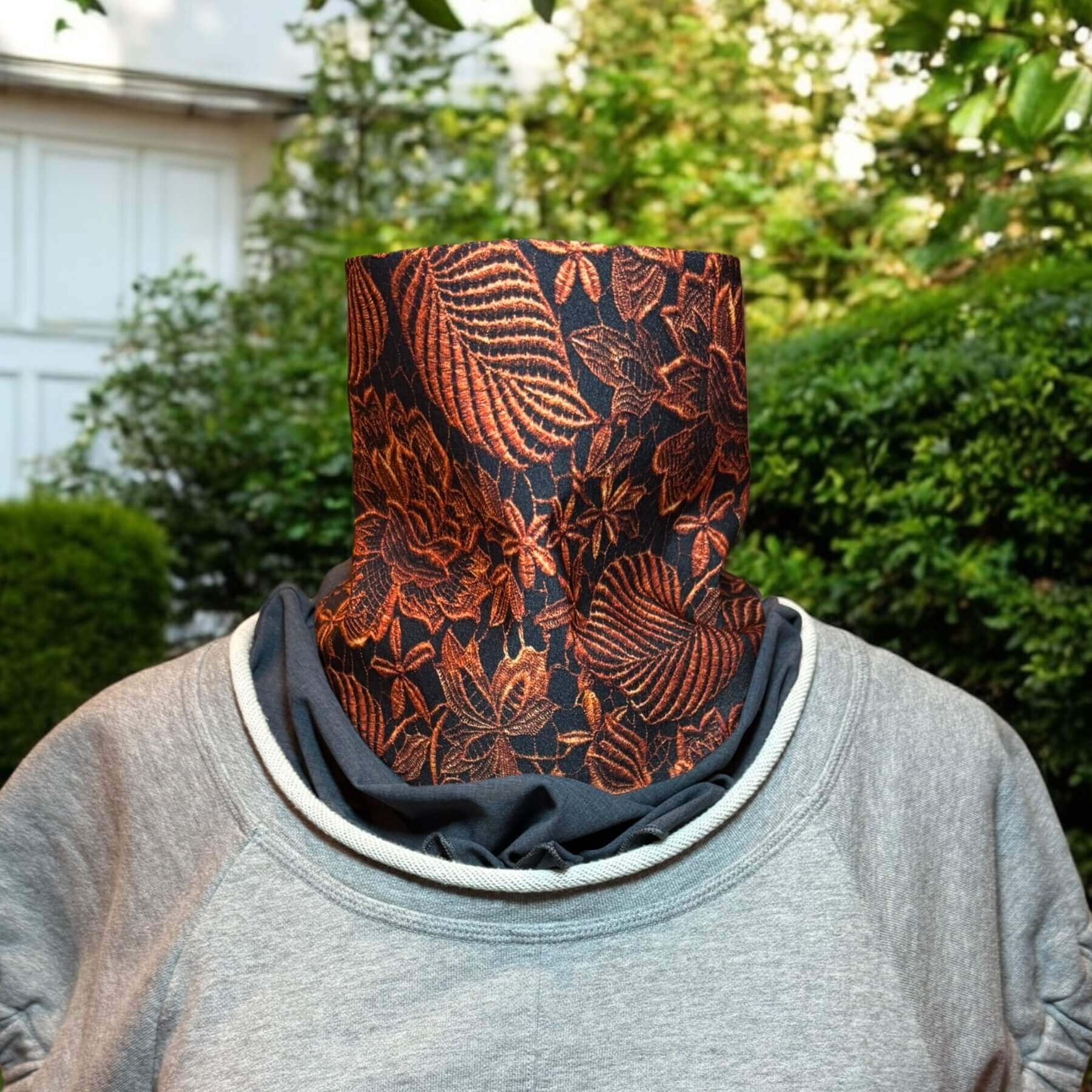 Mannequin dressed in Philip Lim gray sweatshirt with rolled jewel collar, fashioned with Heliades Sun Dickey shown in charcoal gray melange with intricately detailed lace print in copper metallic on black. In background is the backyard with garage, trees and green shrubs.