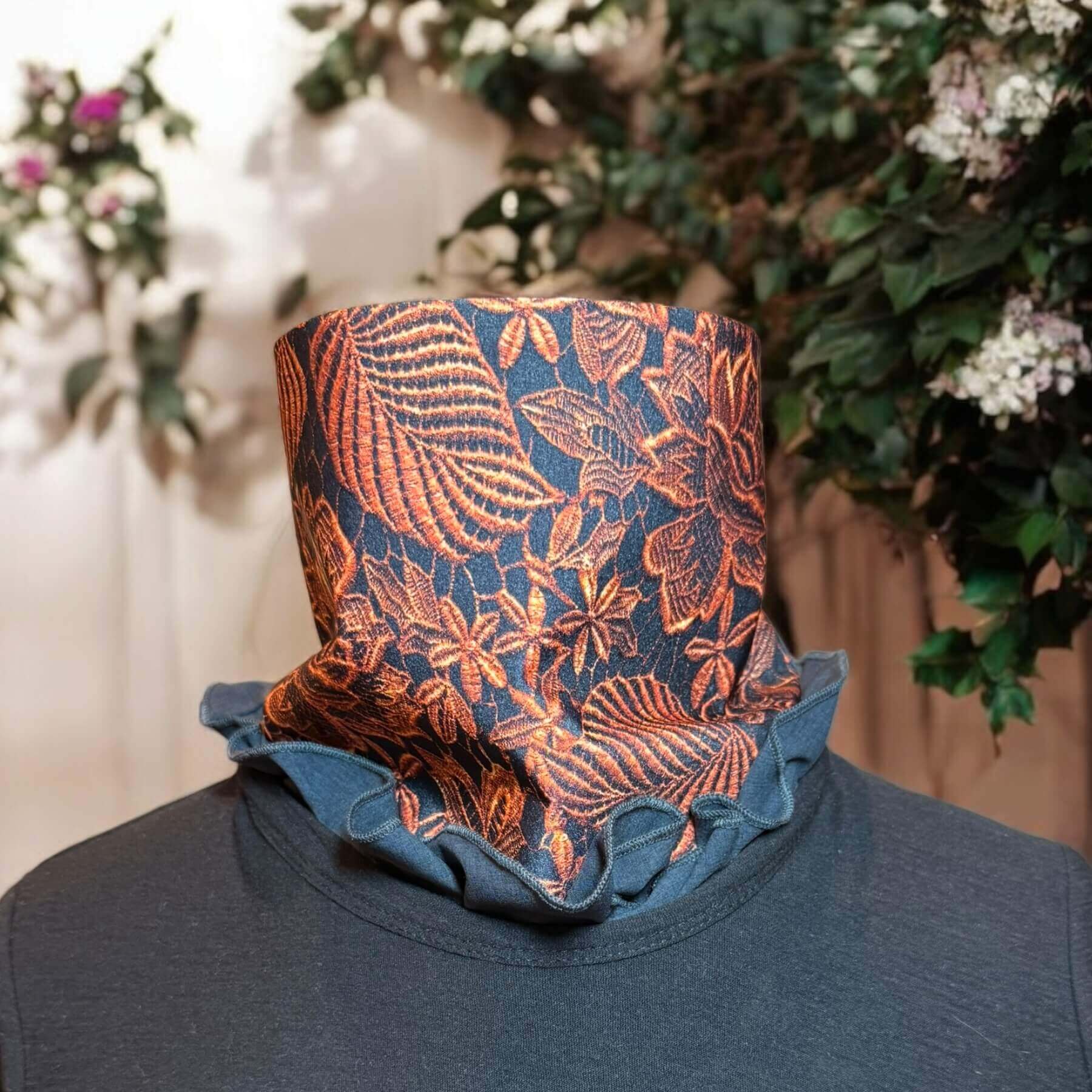 Mannequin with Heliades Sun Dickey shown in charcoal gray melange with intricately detailed lace print in copper metallic on black. The bib of the dickey is tucked into a black t-shirt, ruffled and peeking out of the collar. In background is the backyard with garage, trees and green shrubs.