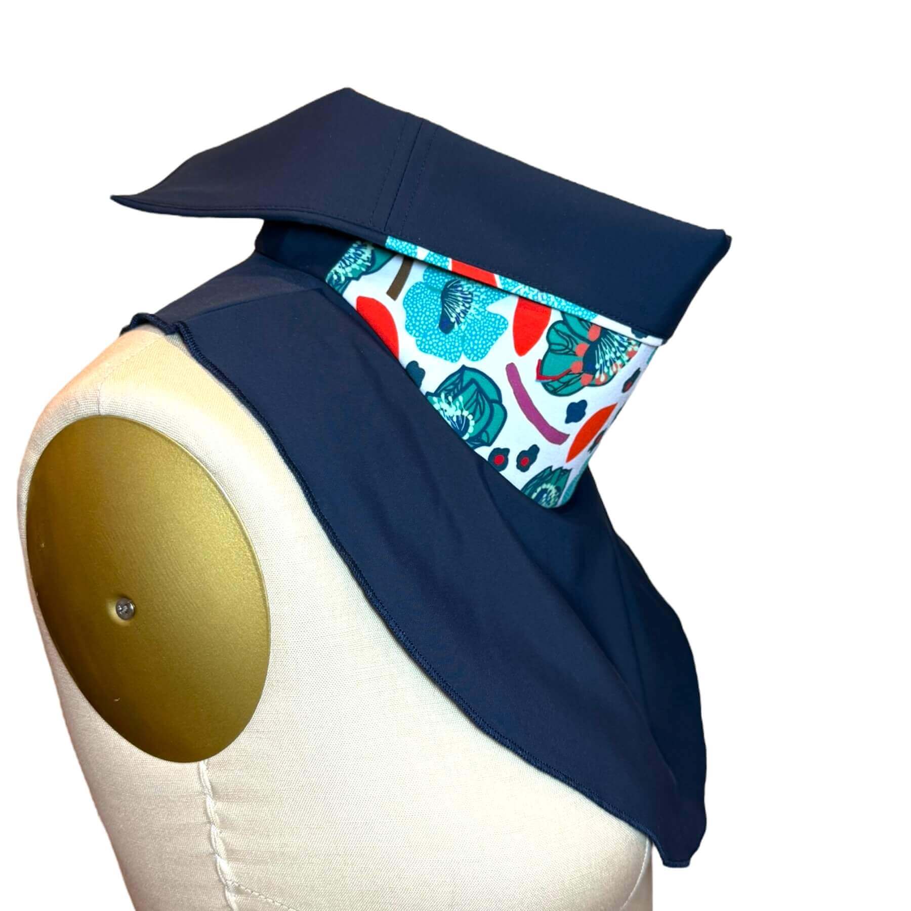 Side view of Sun Dickey shown with collar folded halfway down to reveal navy blue lining which matches the Dickey bib. Colorway shown is navy blue with detailed teal, blue, mint and red flower motif on white print.