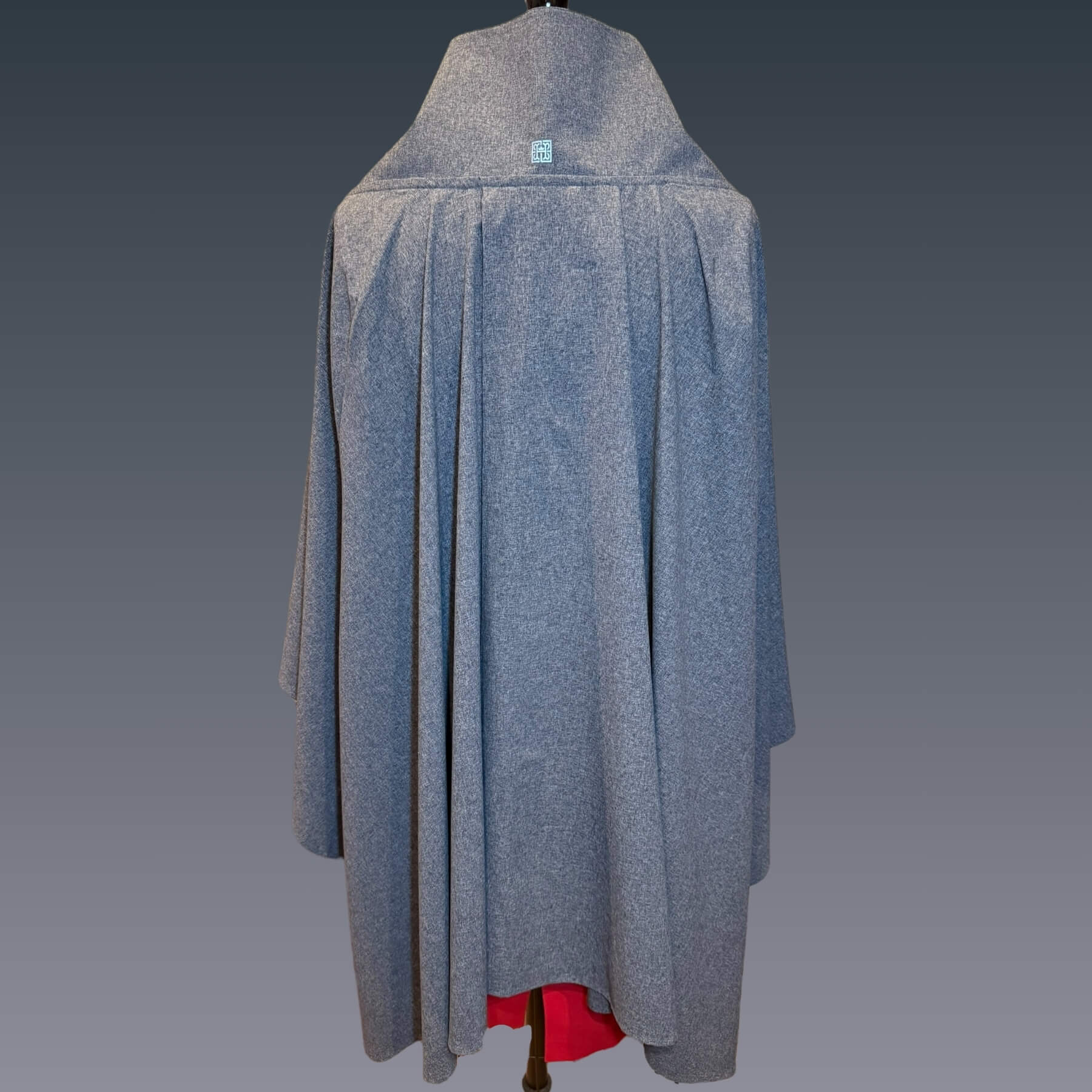 Back view of the Blue Melange Sun Wrap in UPF 50+ fabric, showing its fluid drape and split panel design. Styled on mannequin with red dress against a blue gradient background.