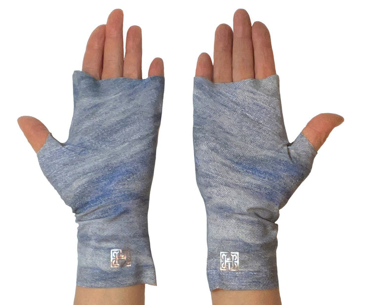 Heliades Sun Protective Clothing lightweight UV sun gloves in stylish patterned UPF 50 fabric. Shown is fashionable, allover blue jeans denim print with blue, gray colors. UV sun covered hands shown in gloves with metallic shimmer pink logo trim