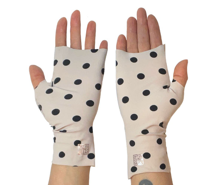 Heliades Sun Protective Clothing lightweight UV sun gloves in stylish patterned UPF 50 fabric. Shown is fashionable, classic polka dot print with ballet pink and black colors. UV sun covered hands shown in gloves with metallic shimmer pink logo trim