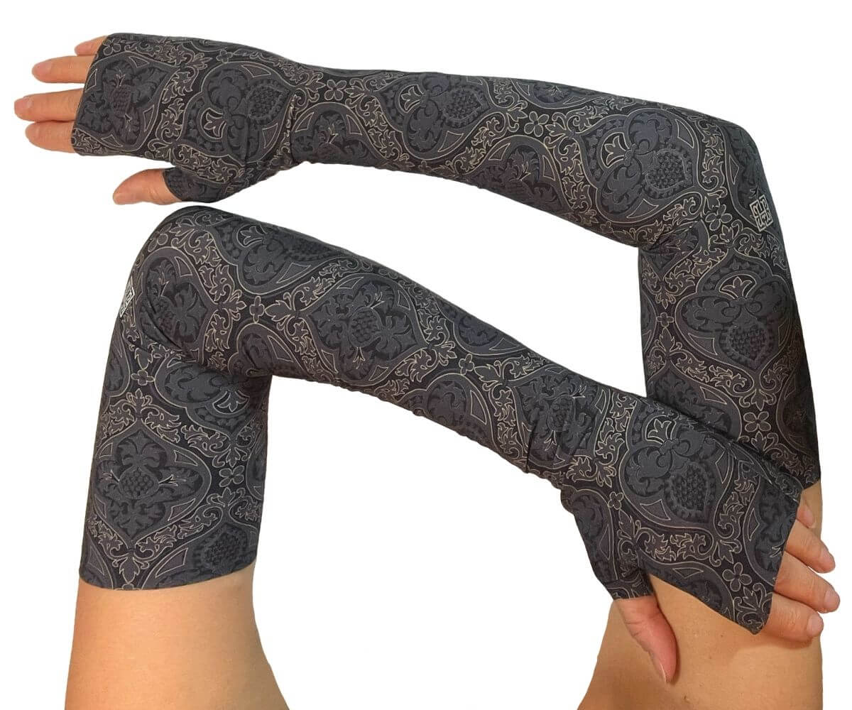 Heliades UPF 50 Sun Protective Clothing UV Arm Sleeves in fashionable, elegant allover black and gold print on a charcoal gray color. UV sun covered arms and hands shown folded in front.