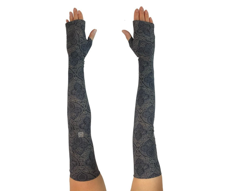 Heliades UPF 50 Sun Protective Clothing UV Arm Sleeves in fashionable, elegant allover black and gold print on a charcoal gray color.  UV covered arms and hands shown outstretched.