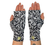 Heliades UPF 50 Sun Protective Clothing UV sun gloves on printed fabric. Shown is fashionable, elegant allover navy blue, white floral pattern. UV sun covered hands shown back with bright green logo trim