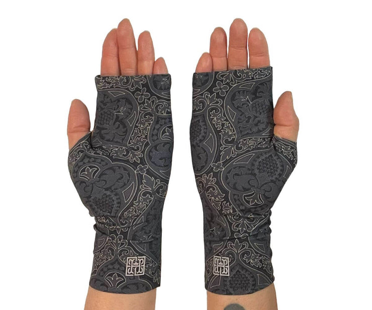 Heliades UPF 50 Sun Protective Clothing lightweight UV sun gloves in stylish patterned fabric. Shown is fashionable, elegant allover print with charcoal gray, black and gold colors. UV sun covered hands shown in gloves with silver reflective logo trim