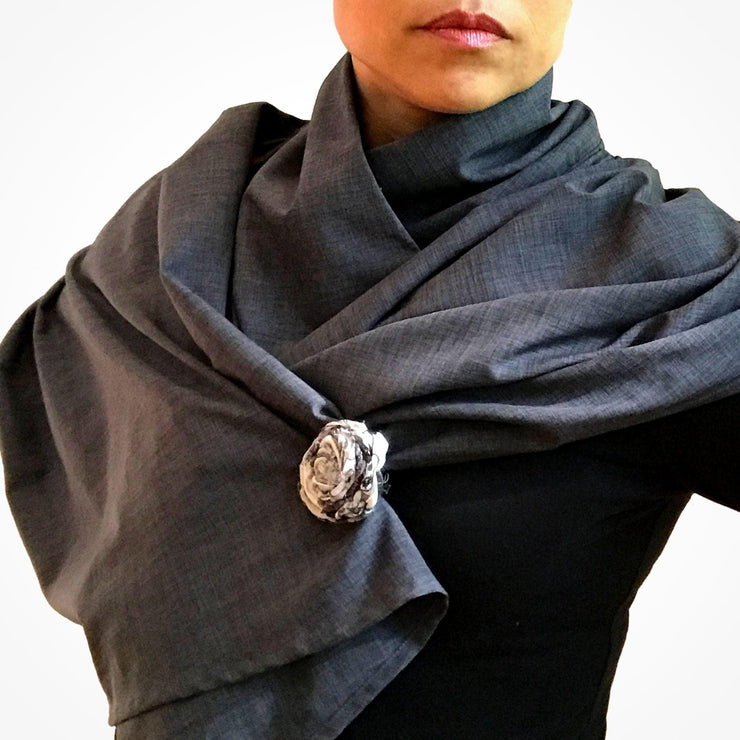 Woman wearing charcoal gray Sol Escape sun protective cape, worn wrapped around shoulders and neck, held in place with hand made fabric spirit flower accessory alligator clip made of upcycled fabric and recycled sari silk in white with black.