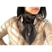 Woman wearing gold down jacket with 70s style flowered shirt in shades of baby blue, pink, green and black. Around her neck is a UPF50+ sun protective scarf in metallic copper and gray sparkling OEKO-TEX fabric, scarf is tied into a cravat.