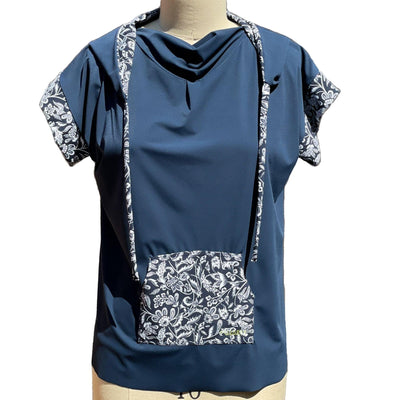 A short sleeved, UPF 50+ hoodie tunic isplaced on a mannequin. The hoodie is true navy blue and the sleeves, inside of the hoodie, string ties and front center pocket are all sewn in a navy with white floral print. The collar is folded down and draped, making nice folds around the jewel neckline. The Hoodie is long, loose and flowing like a tunic with split vents at the hips