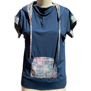 A short sleeved, UPF 50+ hoodie tunic is placed on a mannequin. The hoodie is true navy blue and the sleeves, inside of the hoodie, string ties and front center pocket are all sewn in a painterly houndstooth plaid print. The collar is folded down and draped, making nice folds around the jewel neckline. The Hoodie is long, loose and flowing like a tunic with split vents at the hips