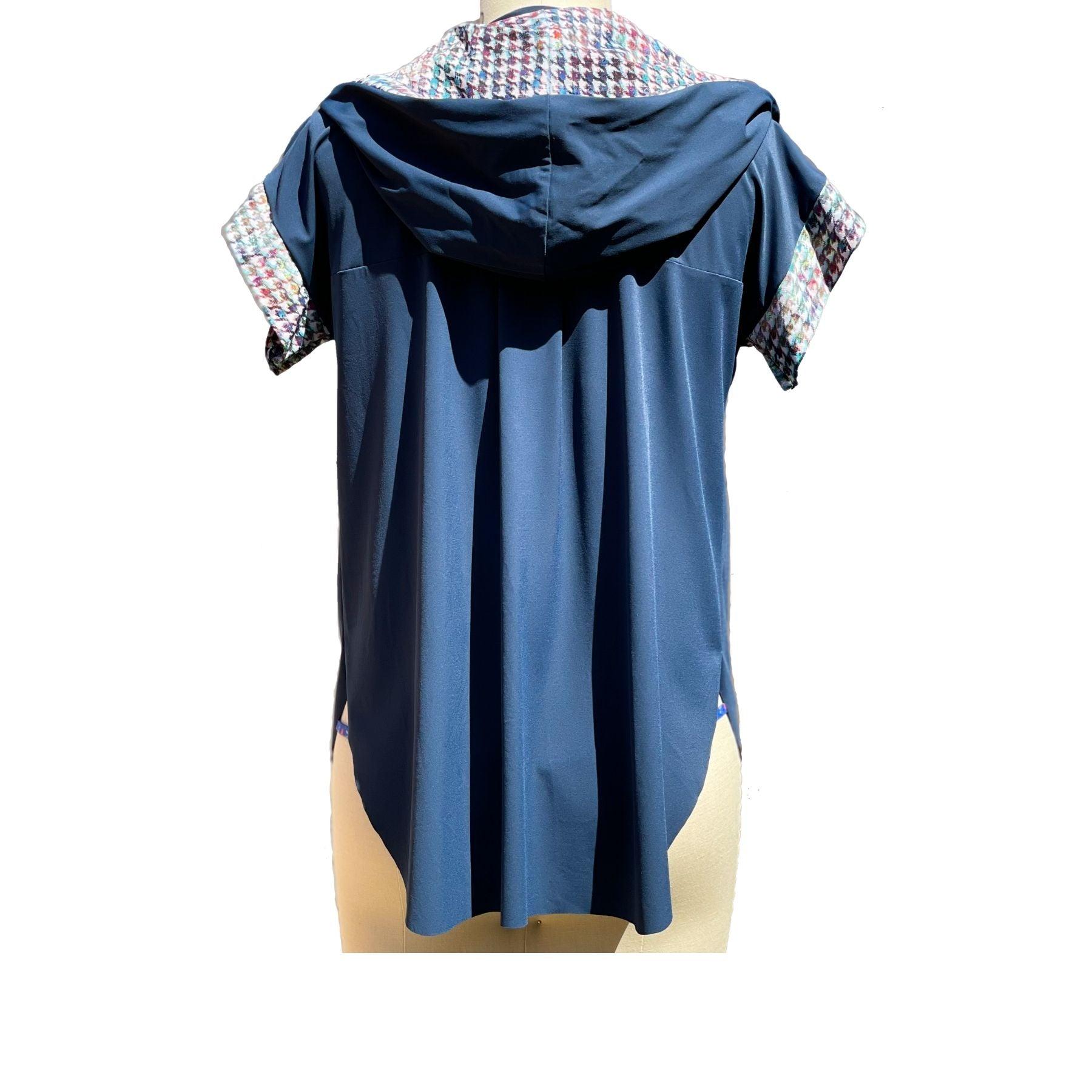 Back view of a short sleeved, UPF 50+ hoodie pullover tunic on a mannequin. The hoodie is true navy blue and the sleeves & inside of the hoodie are all sewn in a painterly houndstooth plaid print. The Hoodie is long, loose and flowing like a tunic with split vents at the hips and a longer length in back for more rear coverage