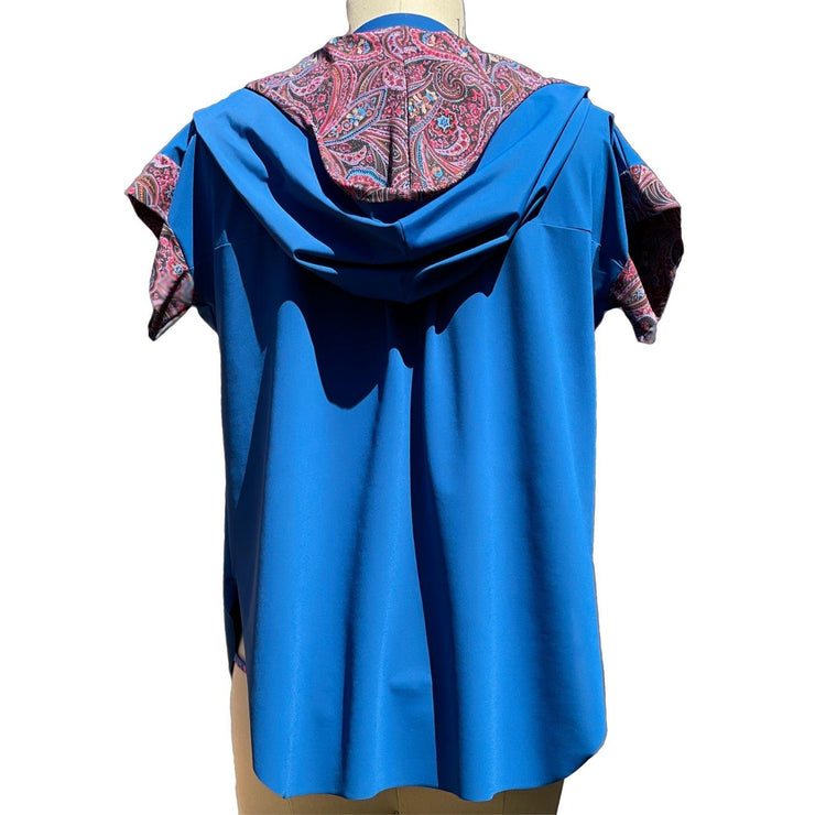 Back view of a short sleeved, UPF 50+ hoodie pullover tunic on a mannequin. The hoodie is deep ocean peacock blue color and the sleeves & inside of the hoodie are all sewn in a paisley print with pink, red, lavender, turquoise colors. The Hoodie is long, loose and flowing like a tunic with split vents at the hips and a longer length in back for more rear coverage