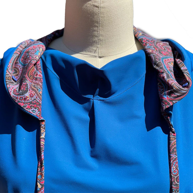 Close up view of UPF 50+ hoodie with collar draped in a jewel neckline. The hoodie is deep ocean peacock blue color and the sleeves & inside of the hoodie are all sewn in a paisley print with pink, red, lavender, turquoise colors.. Hidden, seamless button holes on the collar attach to the hoodie for even more neck coverage. The strings help secure the hood on windy days.