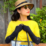 woman wearing sun hat and sunglasses, sunny yellow shirt, holding clear stadium approved bag by drop handles. She is wearing UPF 50+ sun protection arm sleeves in black color
