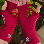 Hands cradle a little flower with salmon and red petals and orange center. Leaves in back ground. On hands are pair of UPF 50+ fingerless sun protection gloves in deep red with silver reflective logos